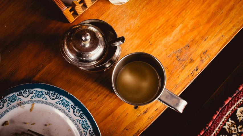 two tea pots, two saucers, a silver coffee pot and a plate on a wooden table