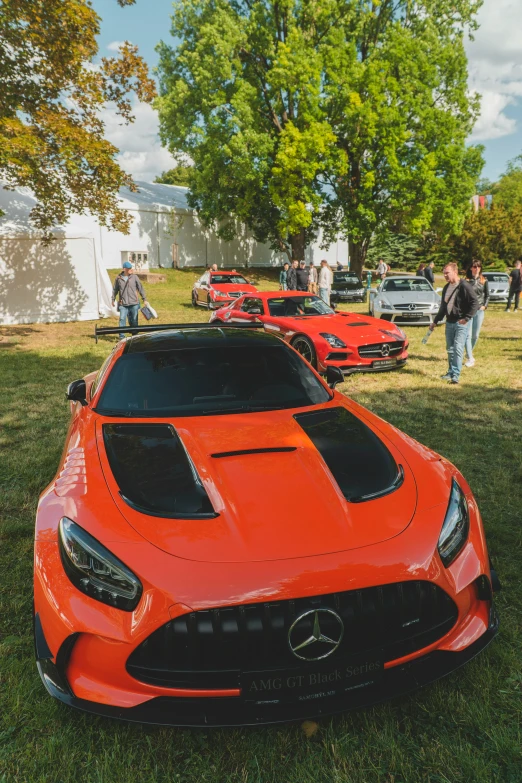 two orange cars are parked near some people in the park