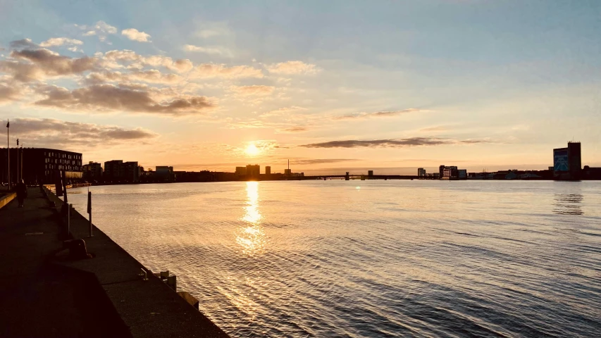 the sun is setting over the water with buildings in the background