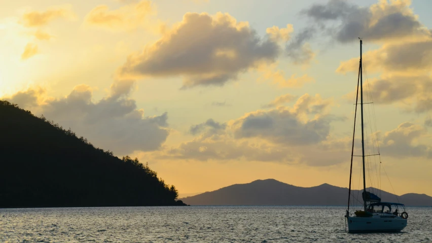 a sailboat in the water at sunset with mountains behind