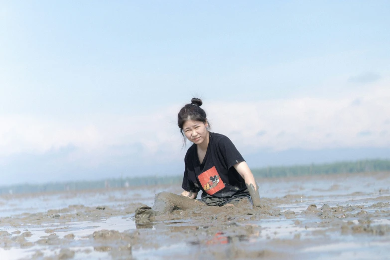 a woman kneeling down in the mud with soing in her hand