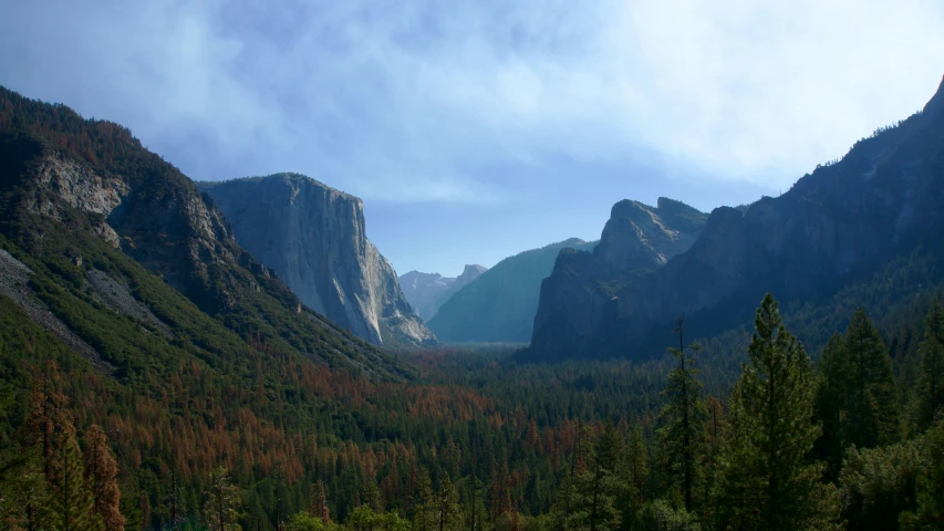 a valley with mountains, trees and sky in the background