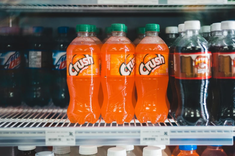 several bottles of orange and red soda on a shelf