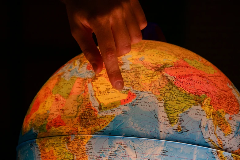 a close up of a person pointing at a world globe