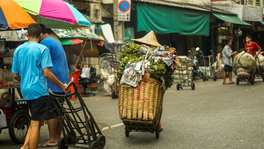 people walk down the street with a cart full of produce