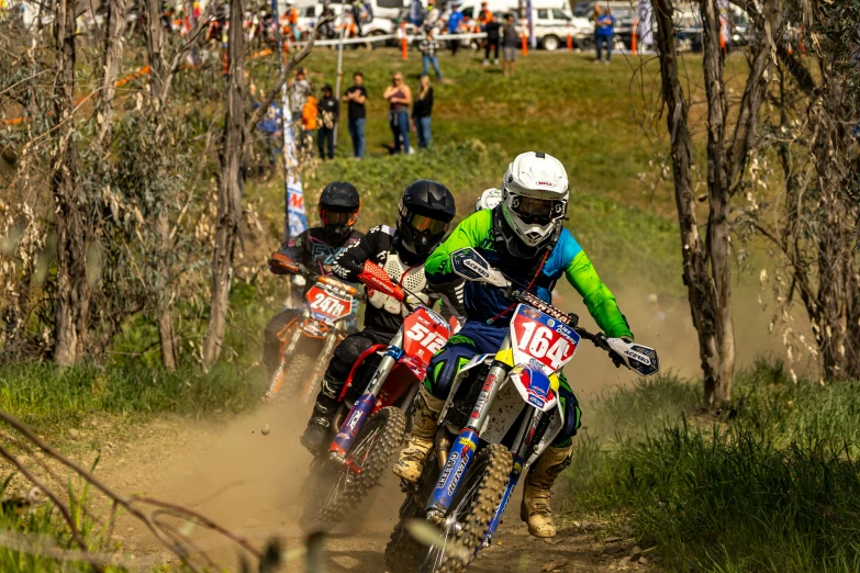 three people racing bikes on a dirt trail