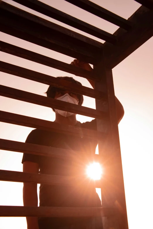 person wearing protective mask against wooden structure at sunset