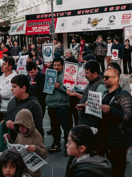 a crowd gathered on a sidewalk, some holding signs and others holding protest signs