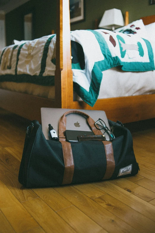 a bag, laptop, and cell phone sit in front of a bed