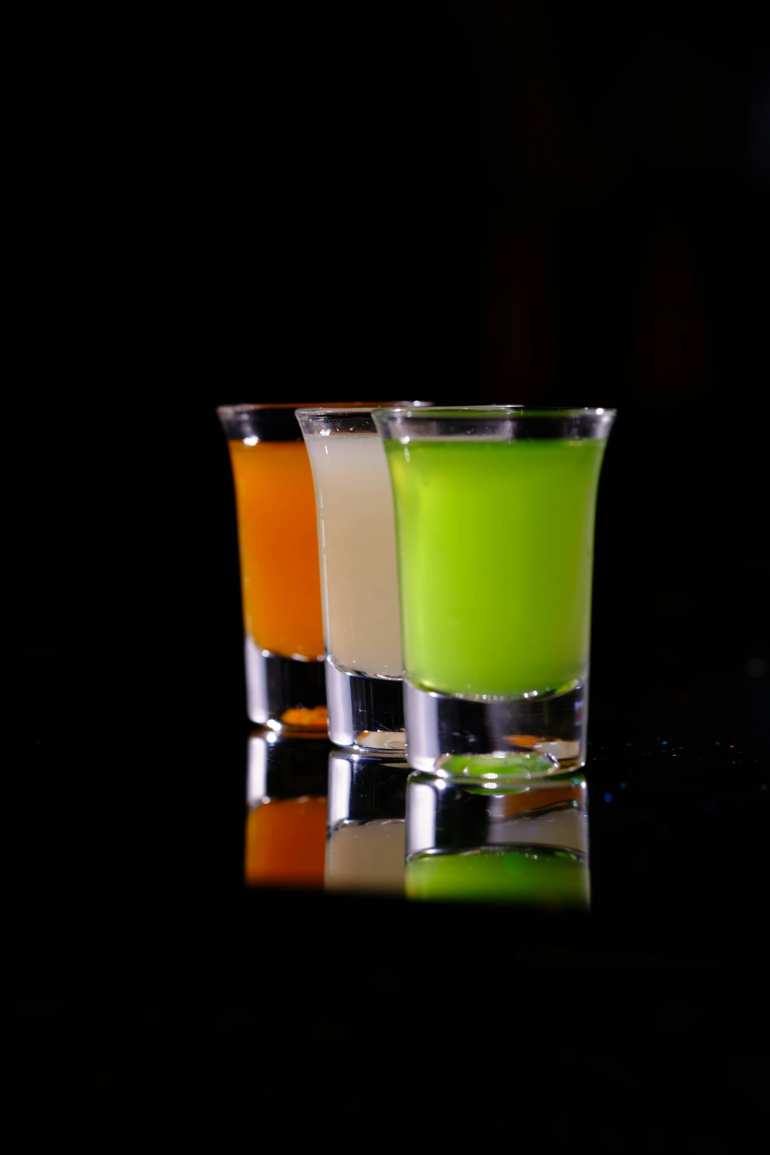 two s glasses with green, orange and white drinks