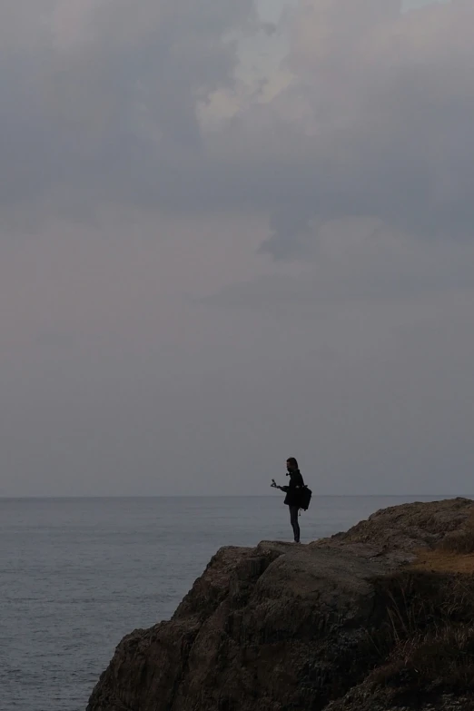 person standing on cliff overlooking ocean with kite