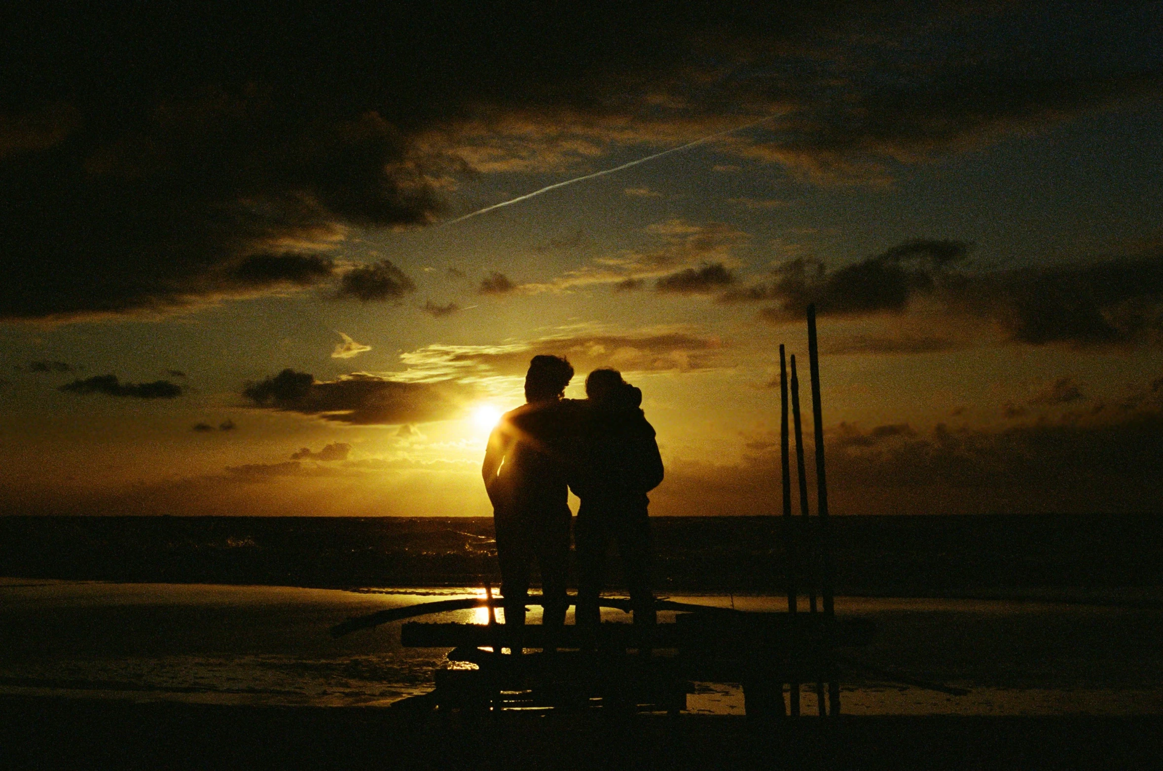 people standing on pier with sunset in background