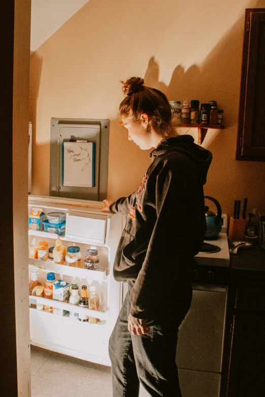 a young woman in jeans and boots looking at a refrigerator