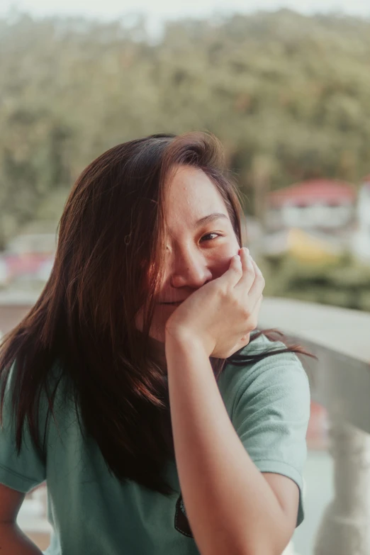 a young asian woman holds her chin to her face, with a smile on her face