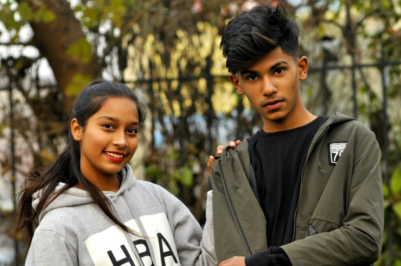 a young man standing next to a teenage girl in front of a gate