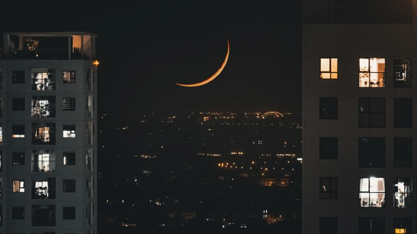 crescent moon in the night sky above buildings