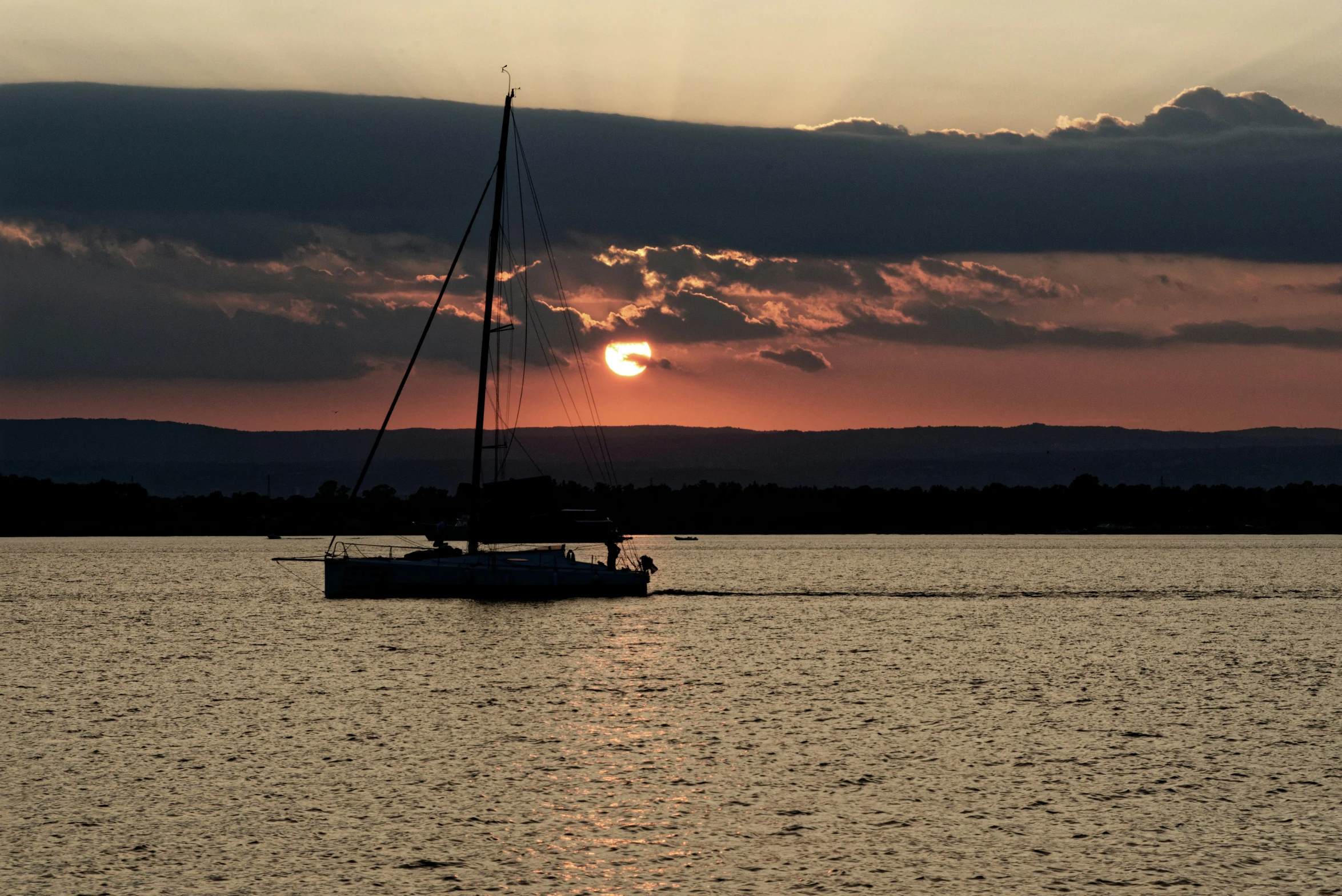 the sun is setting and the sailboat is out on the water