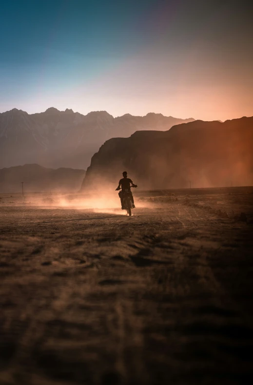 man on dirt bike moving through a desert with mountains in background