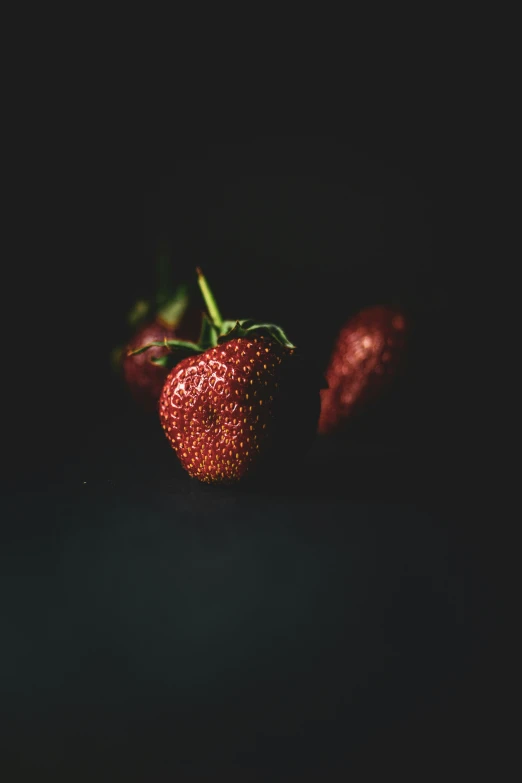 two strawberries with a dark background and one in the center of the po