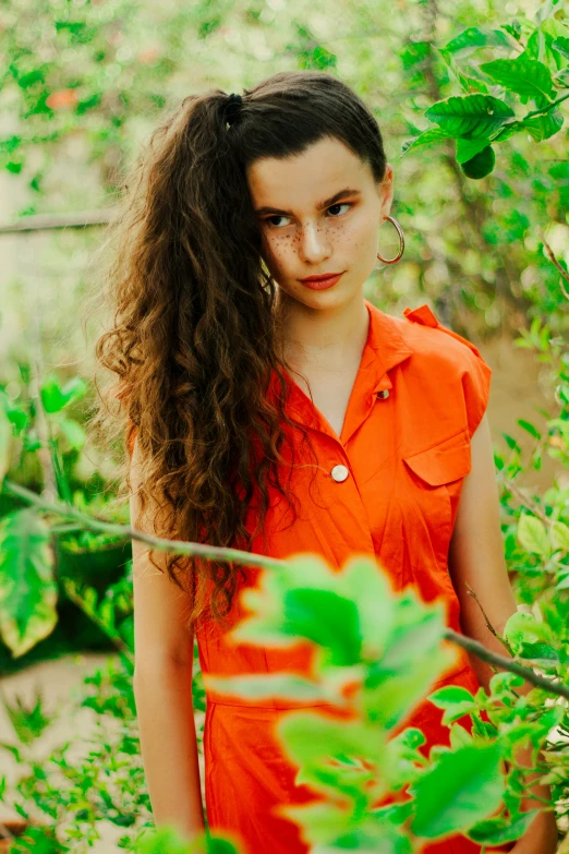 a girl wearing an orange dress stands in green leaves