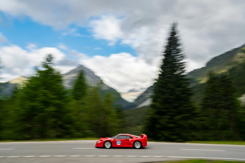 a red sports car driving along the roadway near mountains