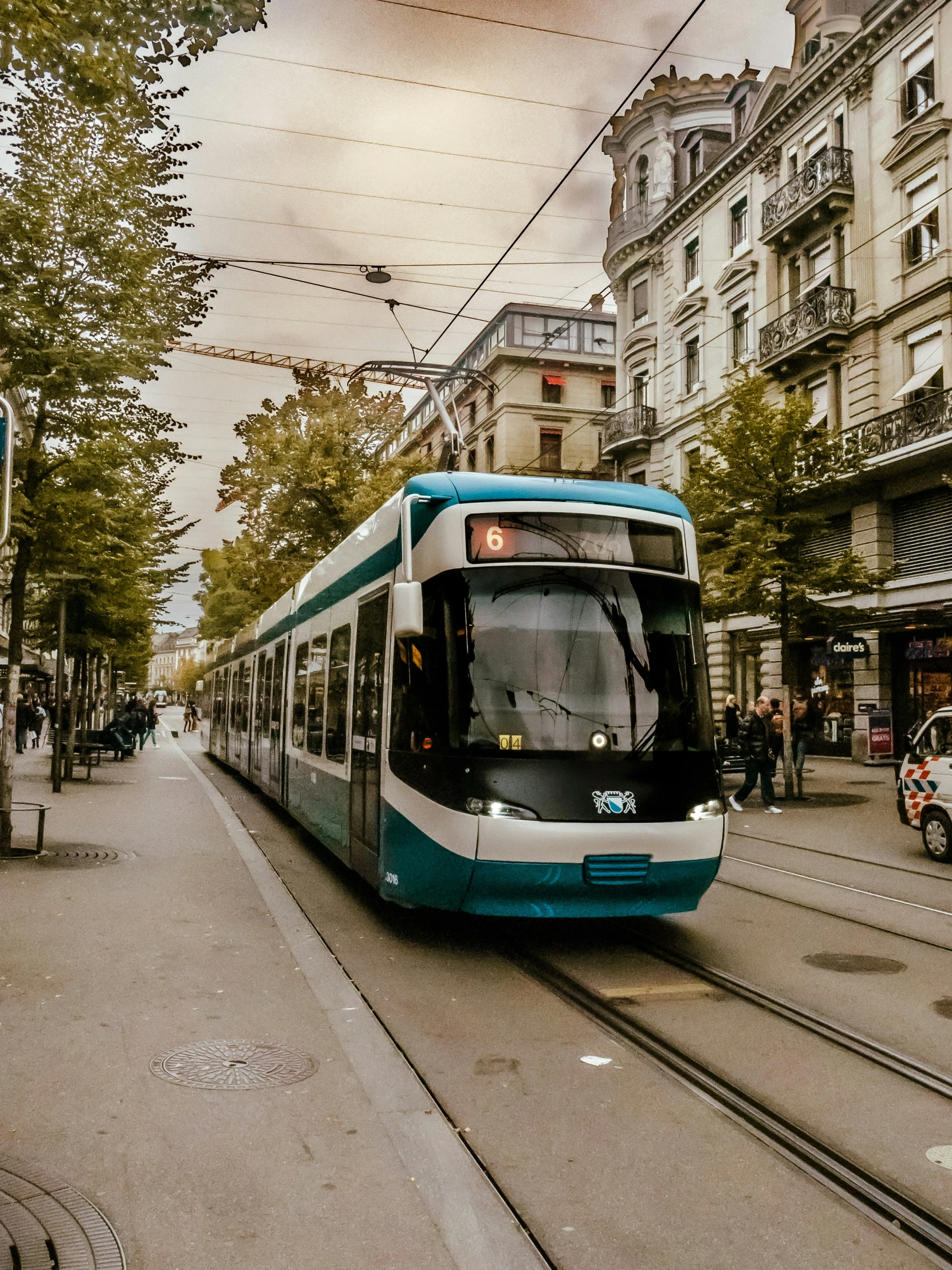 a tram passing down a street with people walking next to it