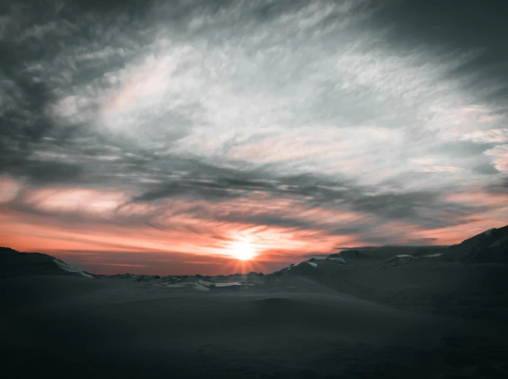 a sunrise over mountains with some very cloudy sky