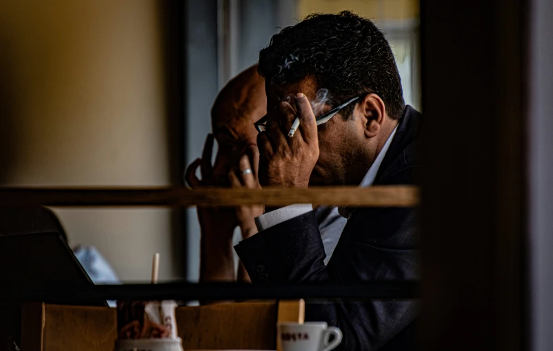 a man sitting at a table holding a cellphone to his ear