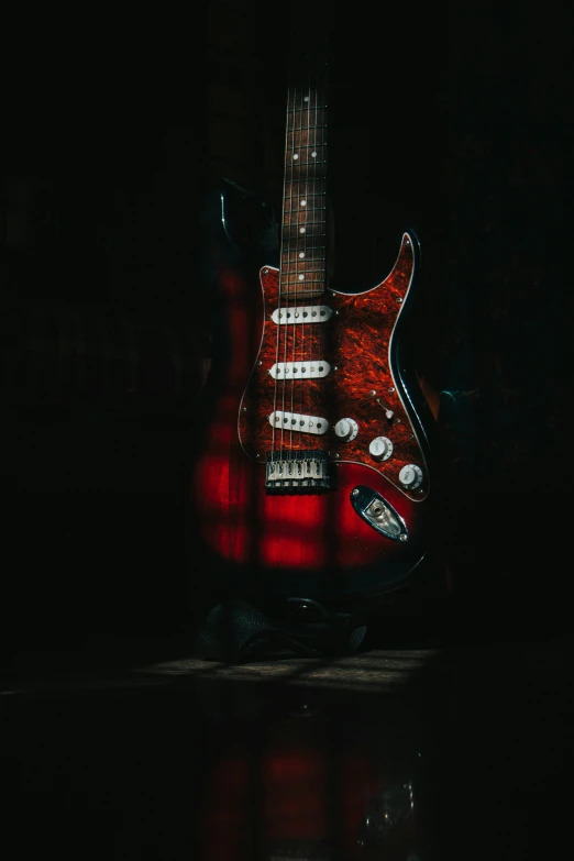 a red guitar laying in a black area