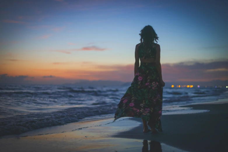 a girl stands on a beach at sunset