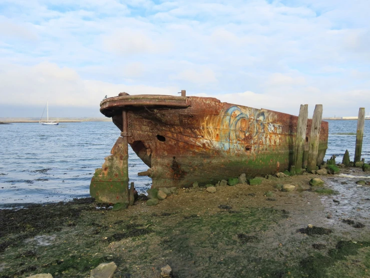a rusted out boat on the shore near a body of water