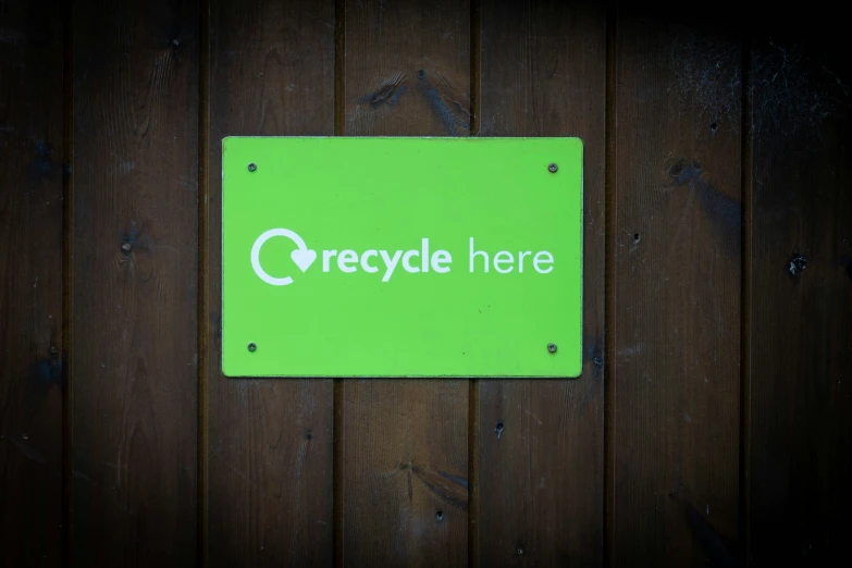 the recycling here sign is attached to a wooden surface