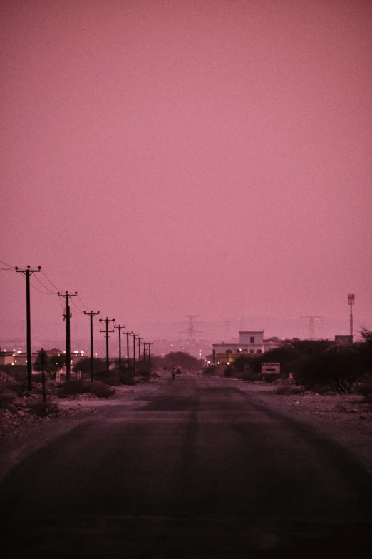 a pink sky and empty road next to some stop lights