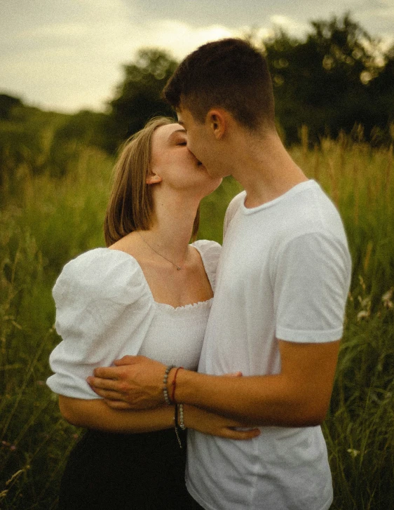 two people kissing in tall grass with trees in the background