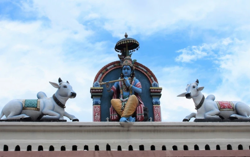 the statues on the roof have cows laying down and a man sitting atop them