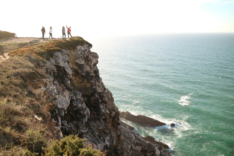 three people stand on the edge of a cliff and look at the ocean