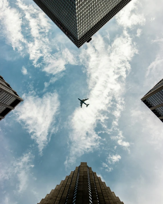 a large commercial plane flying in the sky above tall buildings