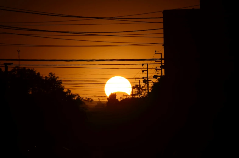 a very beautiful orange ball of sun with power lines