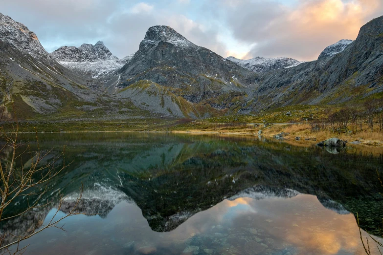 the mountains are covered in snow next to a calm body of water