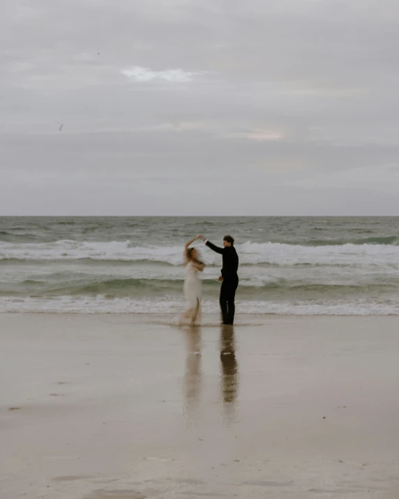 two people standing on a beach near the water