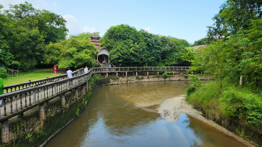 the people are walking across the bridge that leads to the small pond