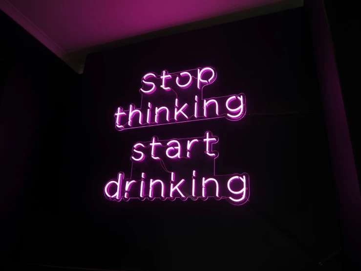 a neon sign reads stop thinking start drinking