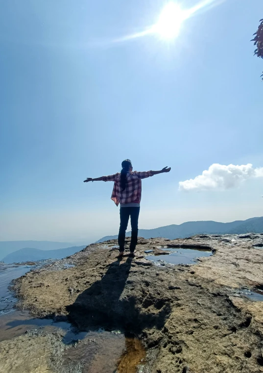 the person is standing on top of a rocky outcropping overlooking the water