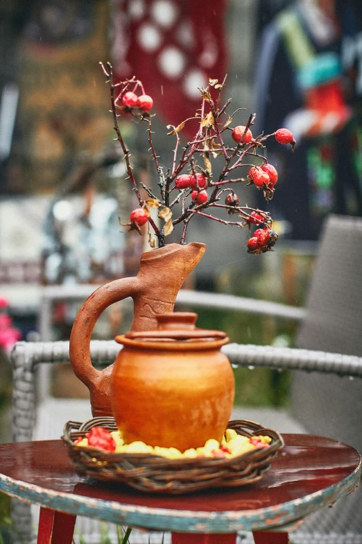 a red vase with berries sits on a table outside