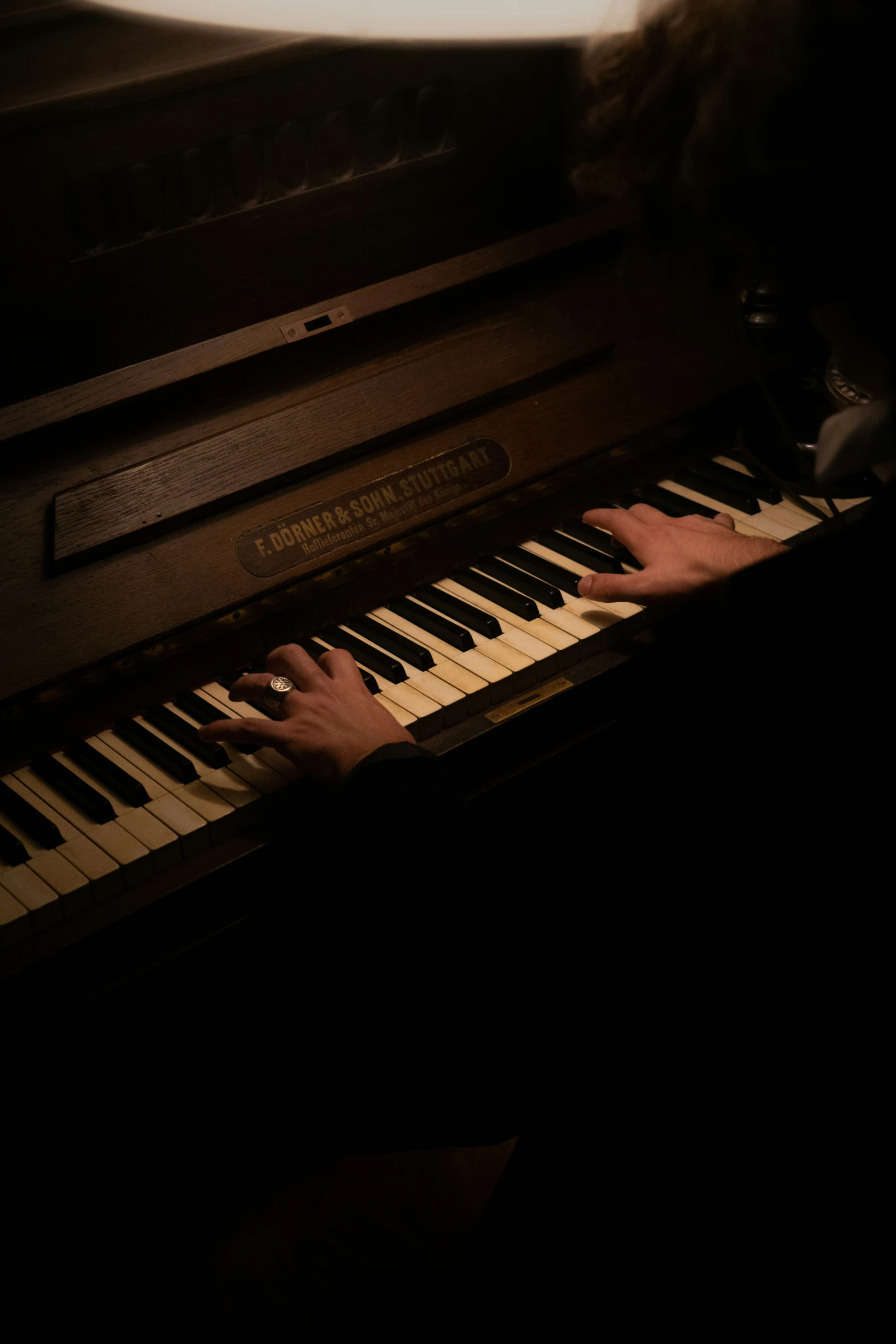 person playing an upright piano with dark lighting