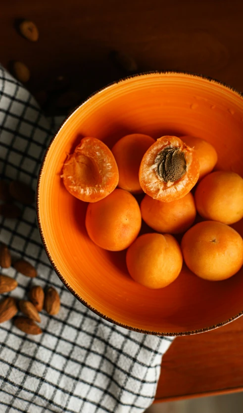 some fruit is in a orange bowl and next to nuts