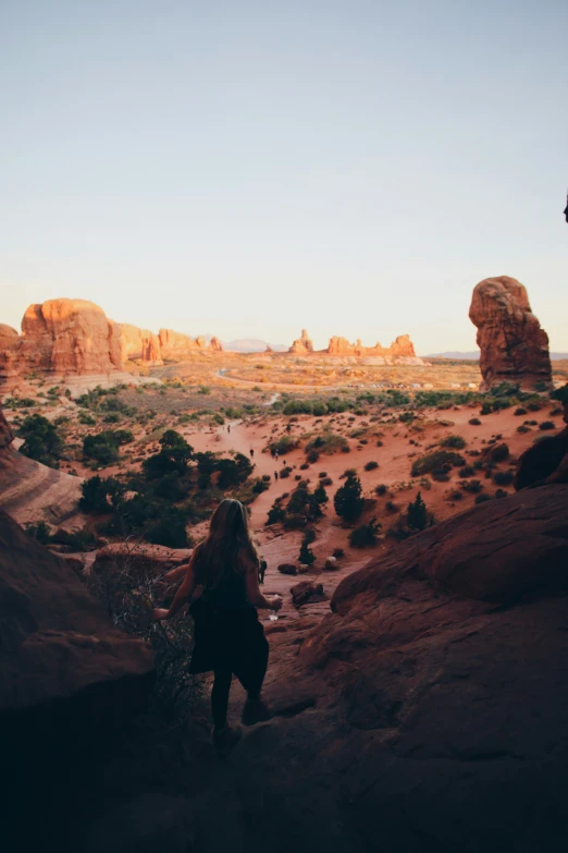 woman in black shirt and jeans walking into desert with large rock formation