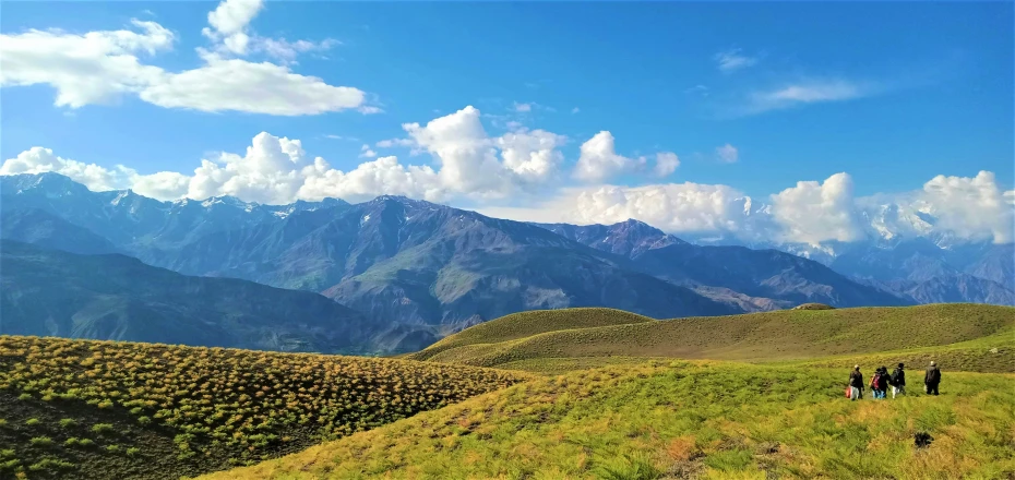 group of people walk on grassy hillside near large mountains