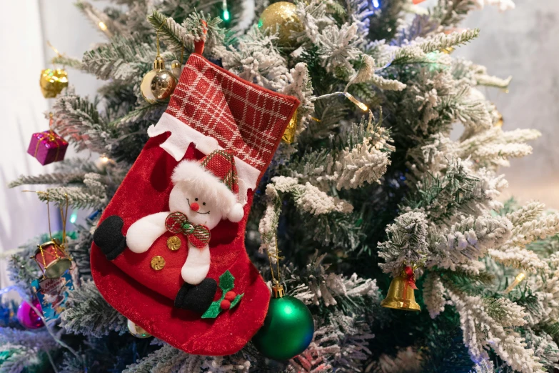 a white and green christmas tree has decorations, such as a red stockings with santa clause and bell