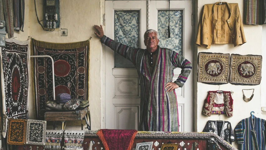 a man leans against the door in front of a store with lots of carpets and rugs